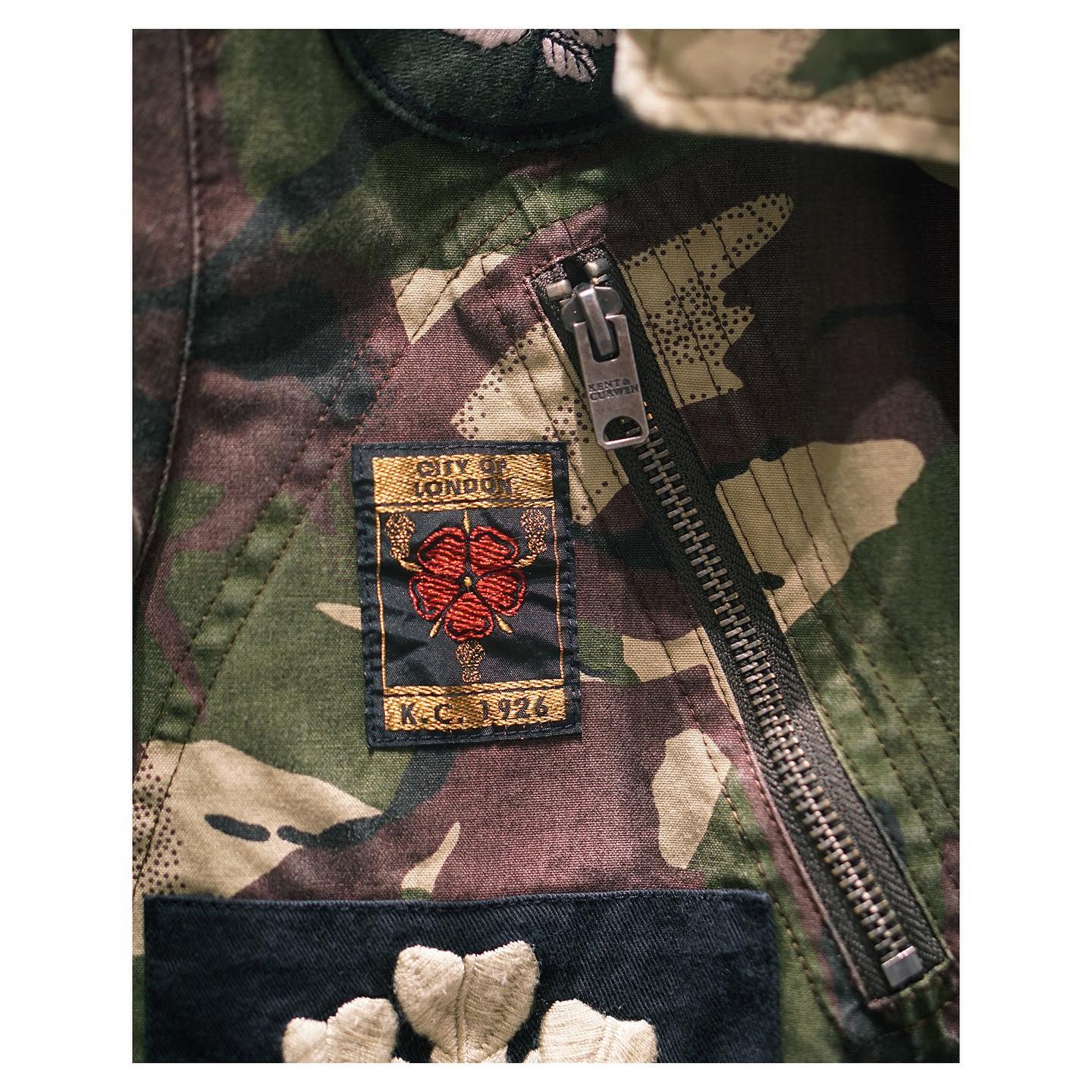 Details of our signature, distinctive Army Field Jacket in camouflage with a selection of house badges. Featuring zipped front pockets, flapped side pockets and a removable hood, this versatile and unique piece gives a nod to our military tradition and heritage.